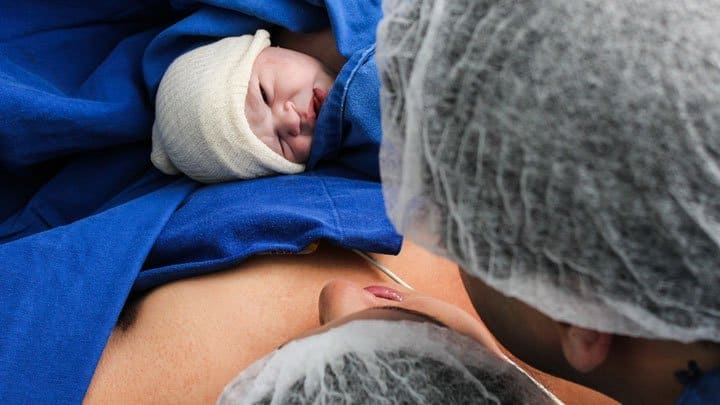 newborn baby on moms belly, dad is watching