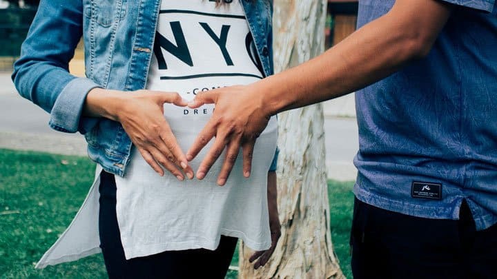 pregnant woman with partner making heart gesture